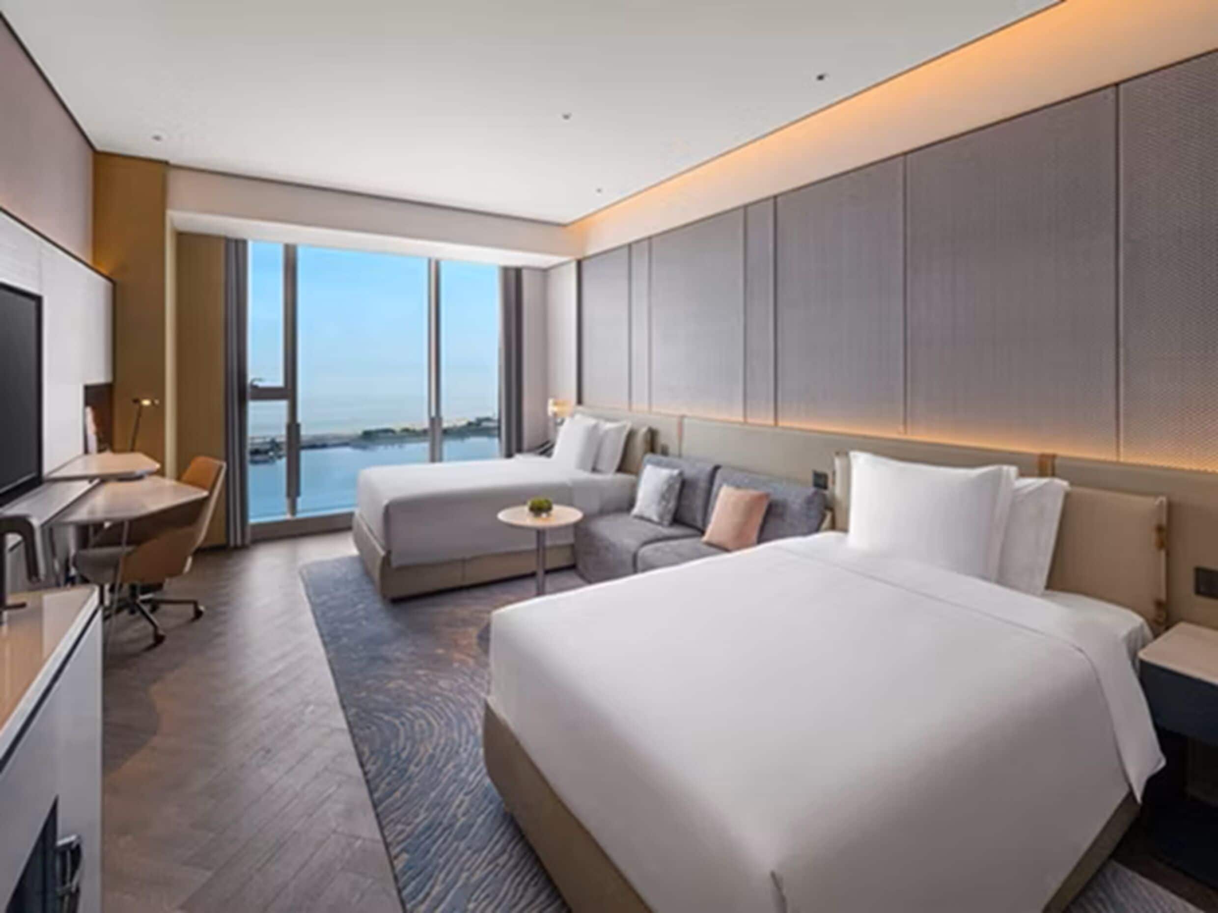 Habitación de hotel moderna con una cama grande, un sofá, una mesita, un escritorio y un televisor.