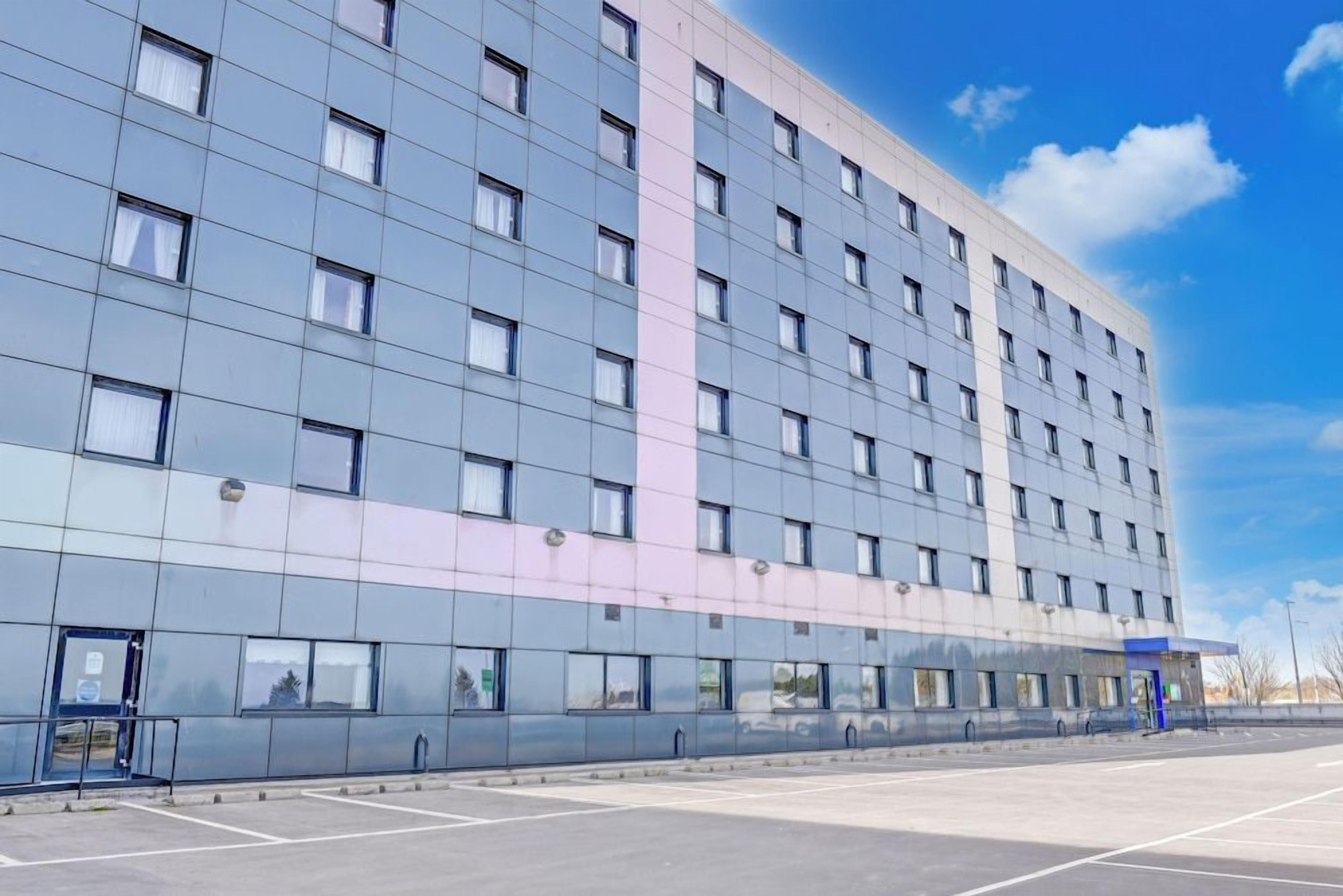 Un hotel moderno con una fachada de ventanas en forma de cuadrícula y un estacionamiento al frente.