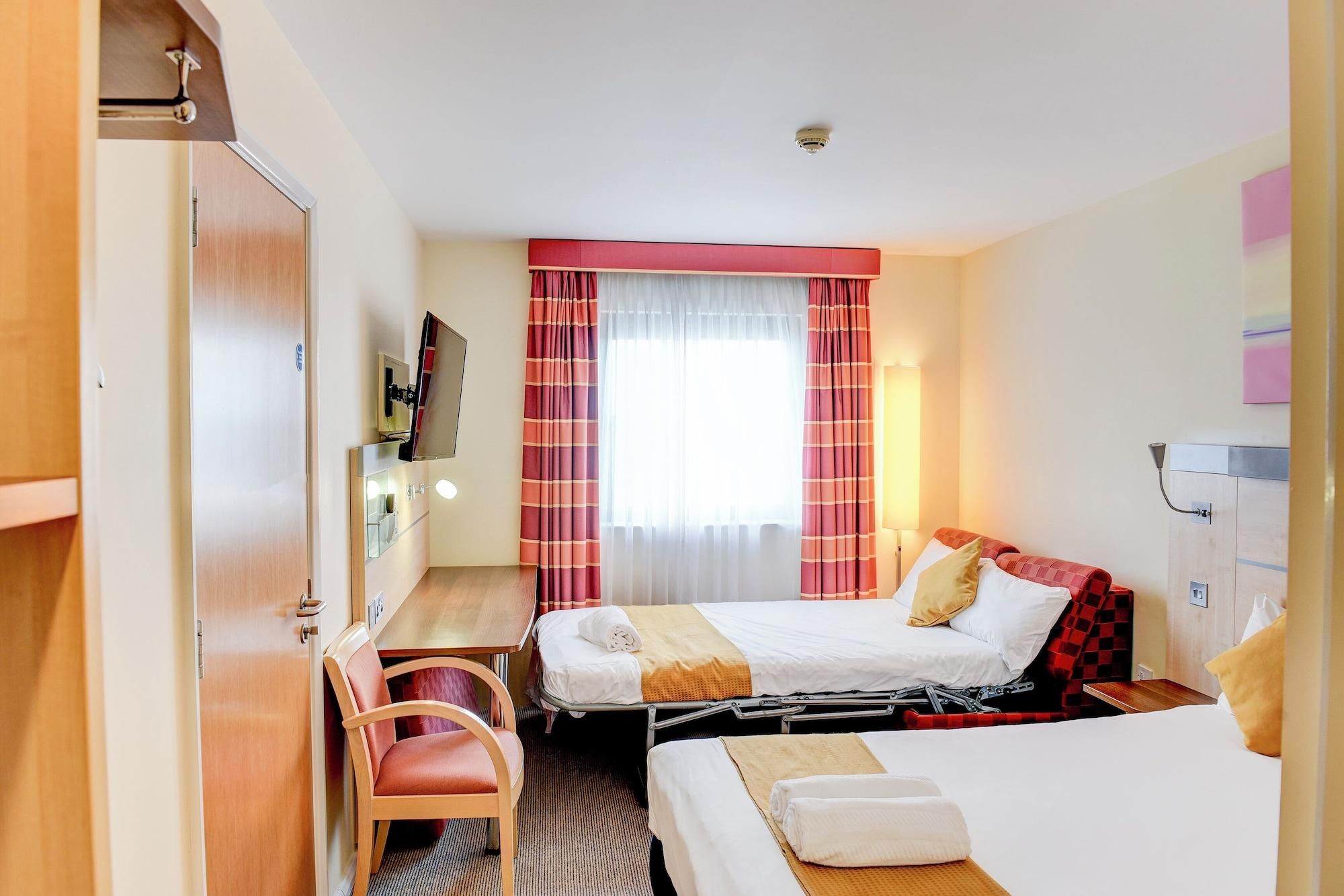 A hotel room with two beds, a desk, a chair, and a mirror.