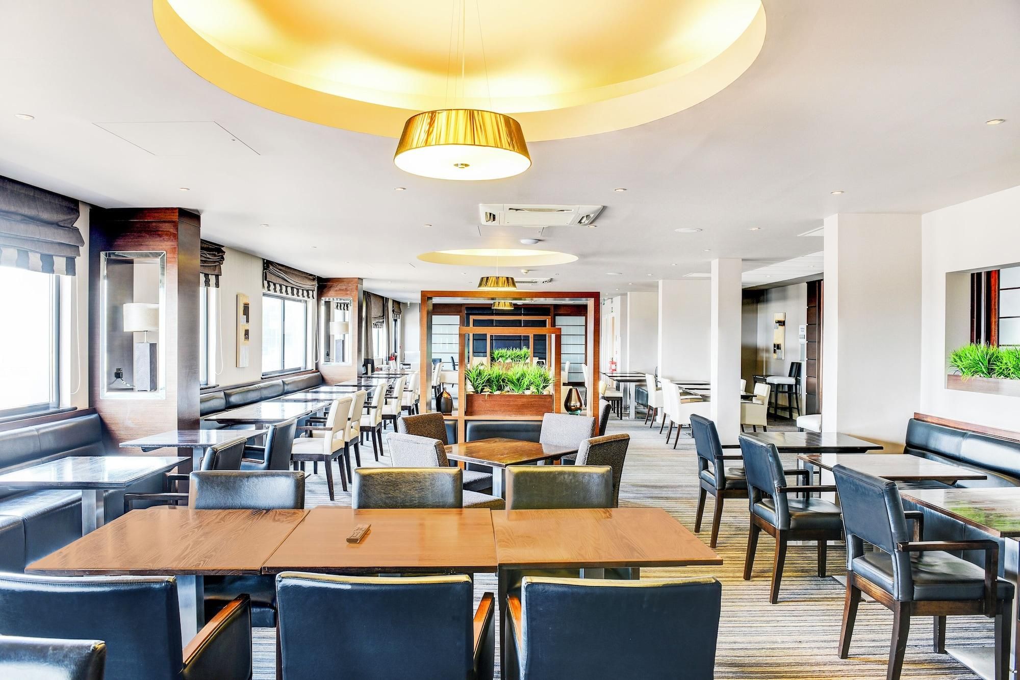 A spacious restaurant with high ceilings, modern lighting, and a mix of seating arrangements including booths and tables.