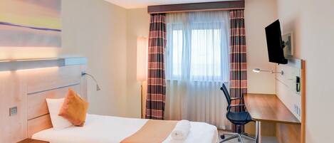 Ein Hotelzimmer mit Bett, Schreibtisch, Stuhl, Fernseher und einem Fenster mit Vorhängen.