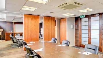 Un salón de conferencias con una gran mesa, sillas, paneles divisorios de madera y una puerta con paneles de vidrio esmerilado.