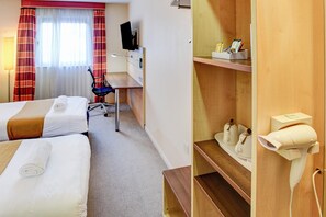 A hotel room with two beds, a desk, a chair, a TV, and a shelf with toiletries.