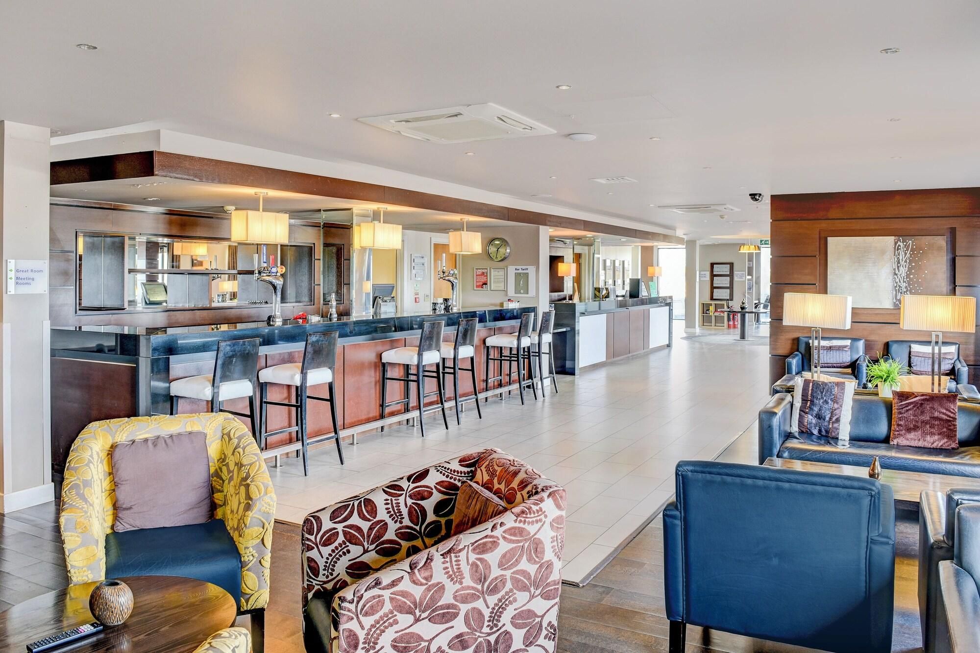 A spacious hotel lobby with a bar area, seating arrangements, and a reception desk.