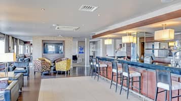 A modern hotel lobby with a bar area, seating, and a large TV screen.