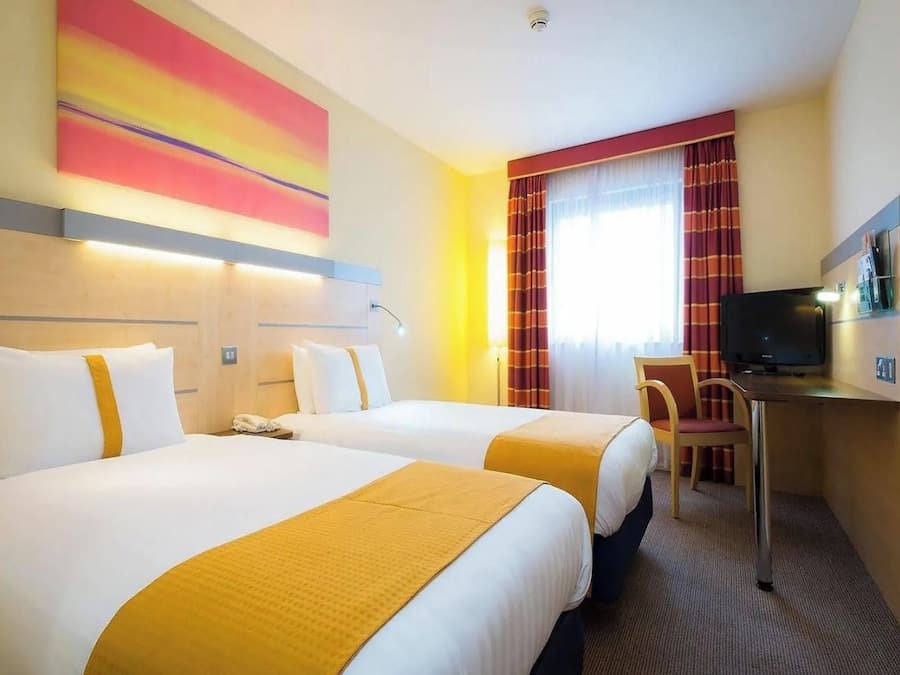 Een hotelkamer met twee bedden, een bureau met een televisie en een raam met gordijnen.