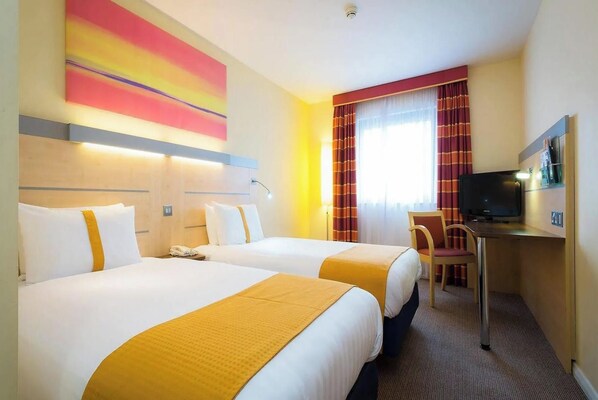 A hotel room with two beds, a desk with a television, and a window with curtains.
