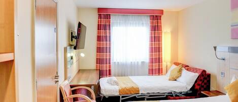 A hotel room with a bed, a desk, a chair, a TV, and a wardrobe.