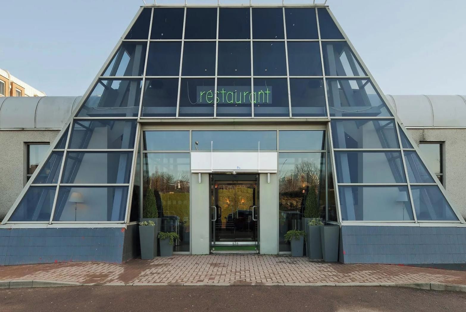 A modern restaurant with a glass facade and a triangular entrance.