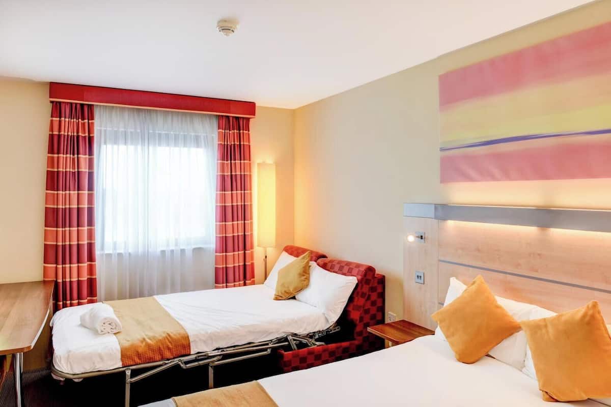 A hotel room with a bed, a desk, and a large window with curtains.