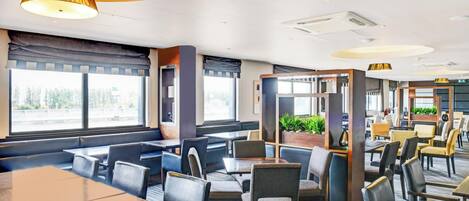 Un restaurante moderno con cabinas y mesas, ventanas amplias y una lámpara de techo cálida.