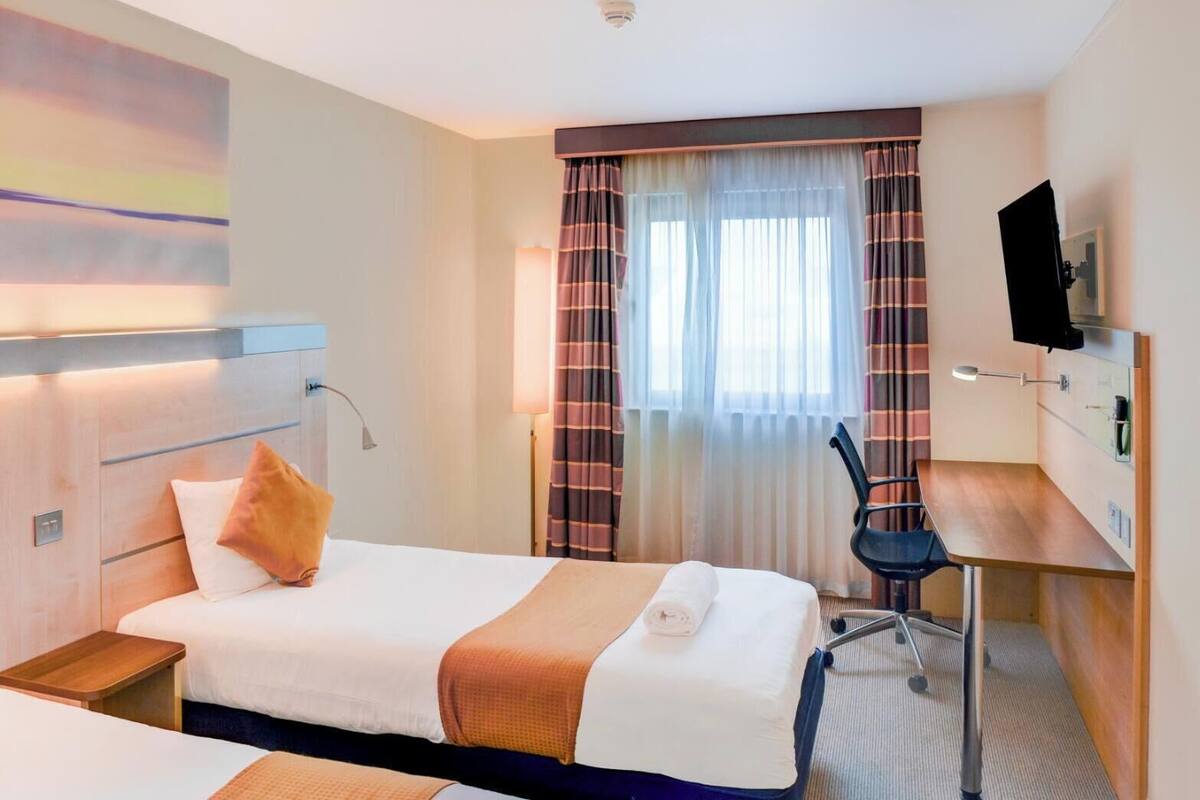 A hotel room with a bed, a desk, a chair, a TV, and a window with curtains.