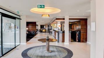 A hotel lobby with a reception desk, a round table with a vase, and a large circular rug.