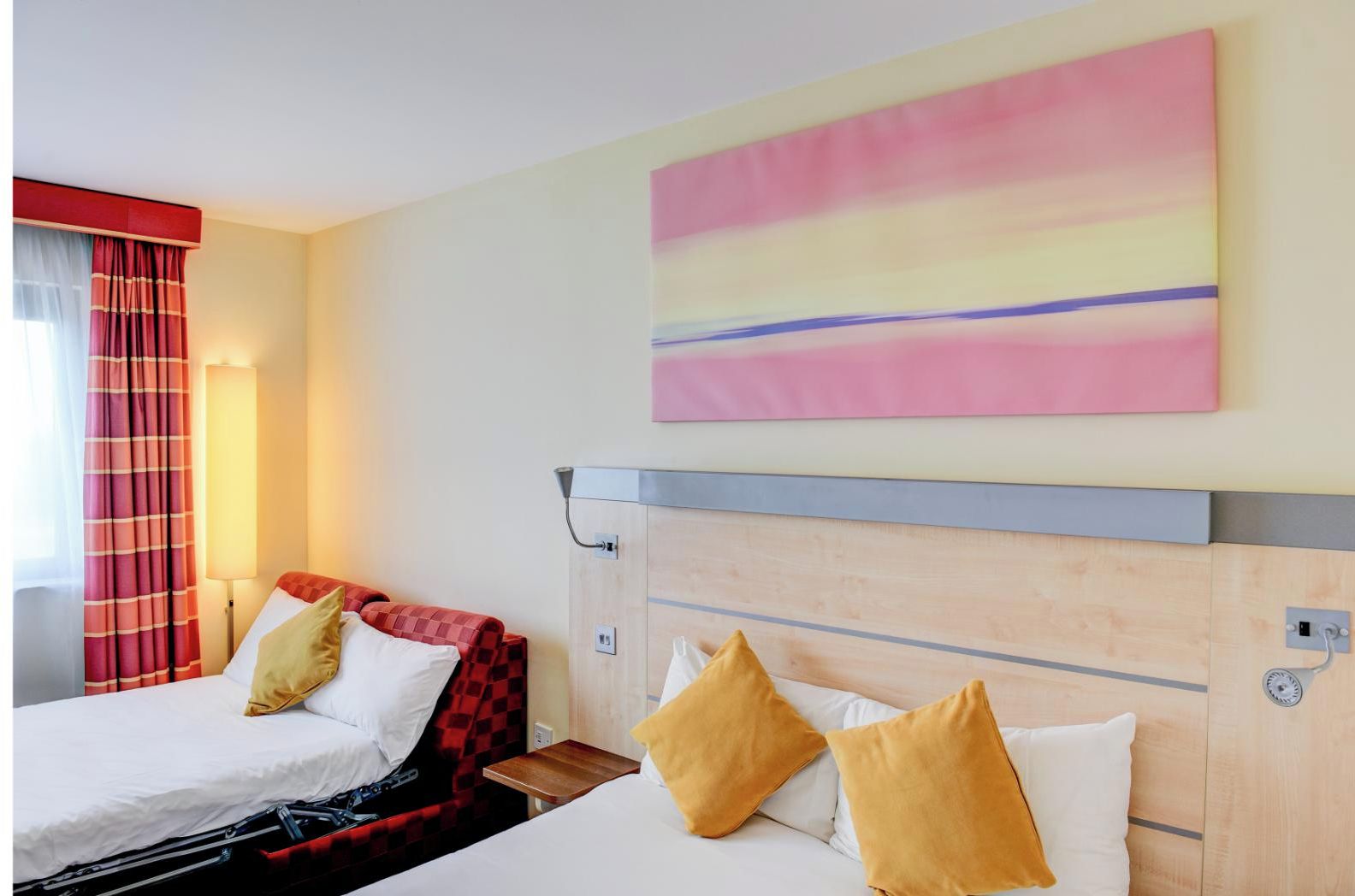 A hotel room with two beds, a large abstract painting, and a red and black checkered bedspread.