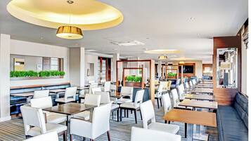 Un restaurante moderno con sillas y mesas blancas, iluminación empotrada y una pared verde cubierta de plantas.