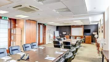 A conference room with a long table, chairs, a whiteboard, a projector screen, and a whiteboard stand.