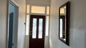 Un pasillo con puerta de madera, un espejo y un candelabro en el techo.