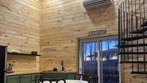 A cozy cabin interior with a wooden interior, a dining area with a table and chairs, a kitchen with green cabinets, and a spiral staircase.