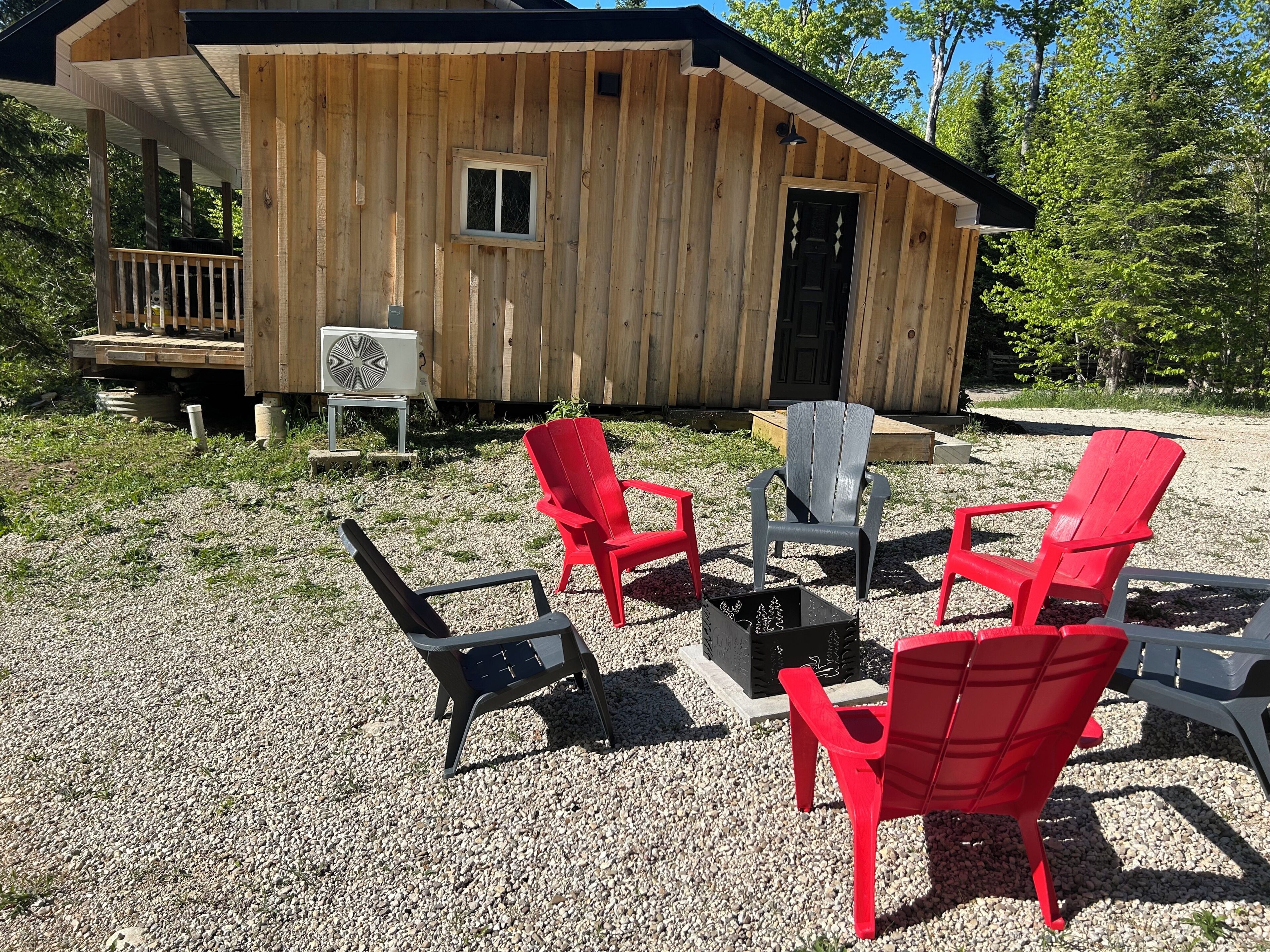 A wooden cabin with a porch, a fan, and four Adirondack chairs.