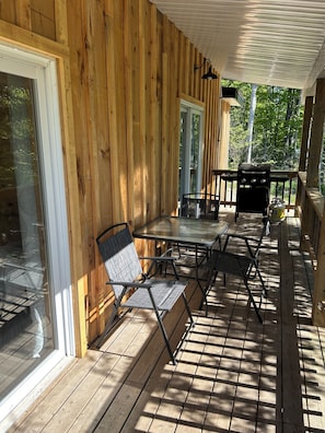A wooden deck with a glass door, a table with chairs, and a grill.
