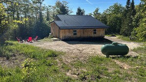 A wooden cabin with a metal roof, surrounded by a forest.