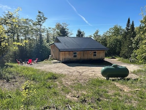 A wooden cabin with a metal roof, surrounded by a forest.