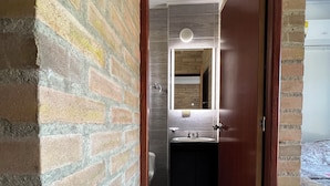 A narrow hallway with a brick wall on one side and a wooden door leading to a bathroom. - The Cayetano House (Cali)