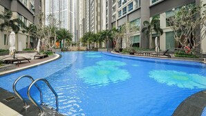 A swimming pool surrounded by high-rise residential buildings, with lounge chairs and palm trees. - Vinhomes Central Park AnAn Apartment (Ho Chi Minh City)