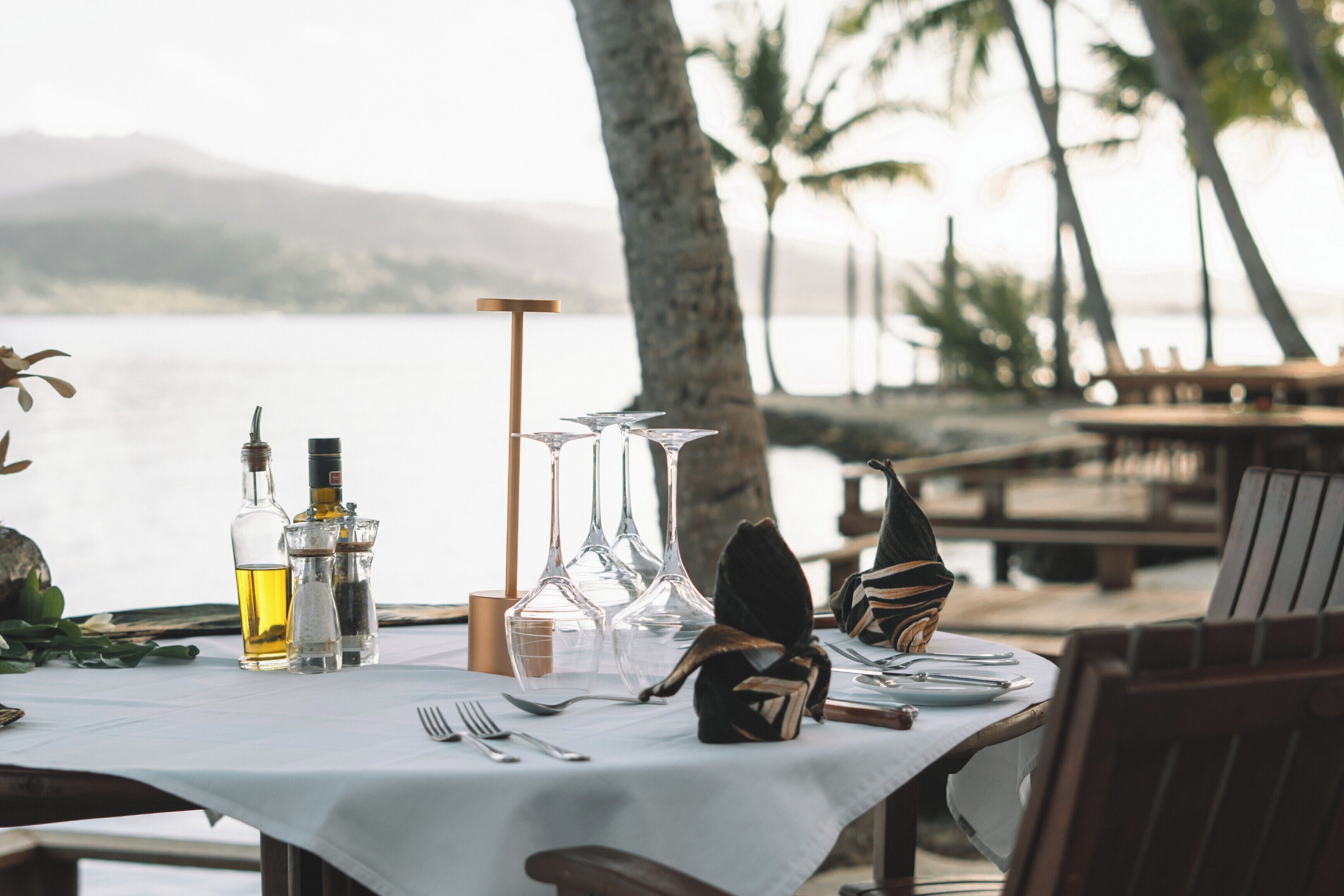 A table set for dining with a view of the water and palm trees.