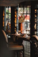 Interior de un restaurante tenuemente iluminado, con una mesa lista para dos personas, una copa de vino y un florero con flores.