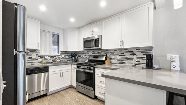 A modern kitchen with white cabinets, stainless steel appliances, and a tiled backsplash.