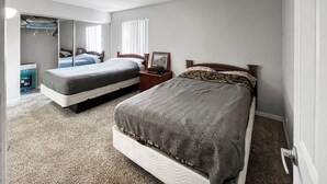 A bedroom with two beds, a wardrobe, and a bedside table with a lamp.