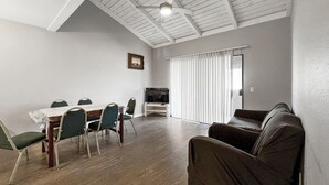 A room with a dining table, chairs, a sofa, a ceiling fan, and a TV.