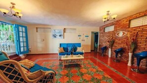 Un vaste espace de vie agrémenté d’un canapé bleu, de fauteuils en osier et d’un tapis à motifs.