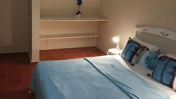 A bedroom with a bed, pillows, a nightstand, and a wall-mounted shelf.