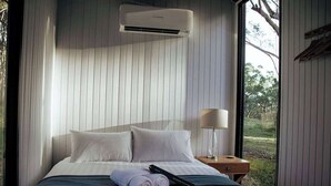 Un dormitorio con cama, almohadas, una mesita de noche con lámpara y un equipo de aire acondicionado.