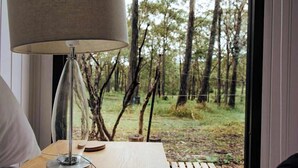 Una habitación con una mesa de madera, una lámpara y vistas a un bosque a través de una ventana.