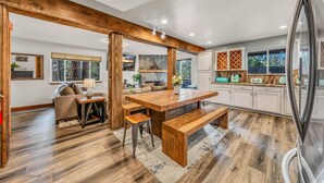 A spacious kitchen with a wooden dining table, benches, and a large island. There are white cabinets and a refrigerator. - Kings Beach Retreat | Hot Tub & Game Loft (Kings Beach)