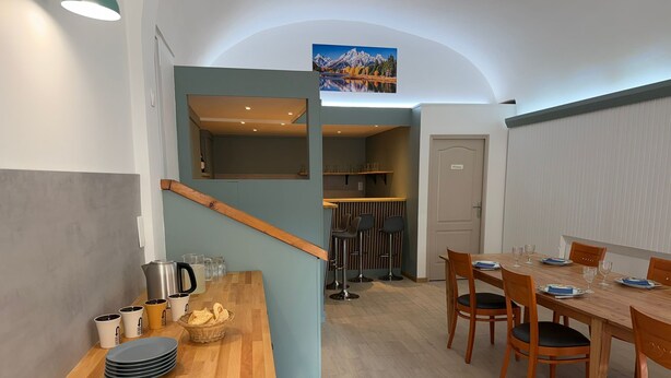 A modern kitchen with a wooden countertop, a cutting board, and a kettle. There is a dining area with a wooden table and chairs.
