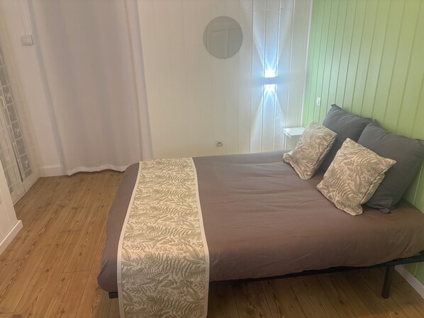 Une chambre à coucher avec un lit, deux oreillers, une fenêtre avec des rideaux et un mur vert.
