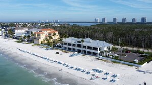 A beachfront hotel with multiple buildings, a sandy beach with umbrellas, and a parking area.