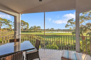 A balcony with a glass table and wicker chairs, overlooking a golf course.