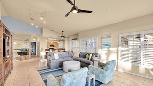 A spacious living room with a gray sectional sofa, blue patterned armchairs, a round ottoman, and a dining area in the background.