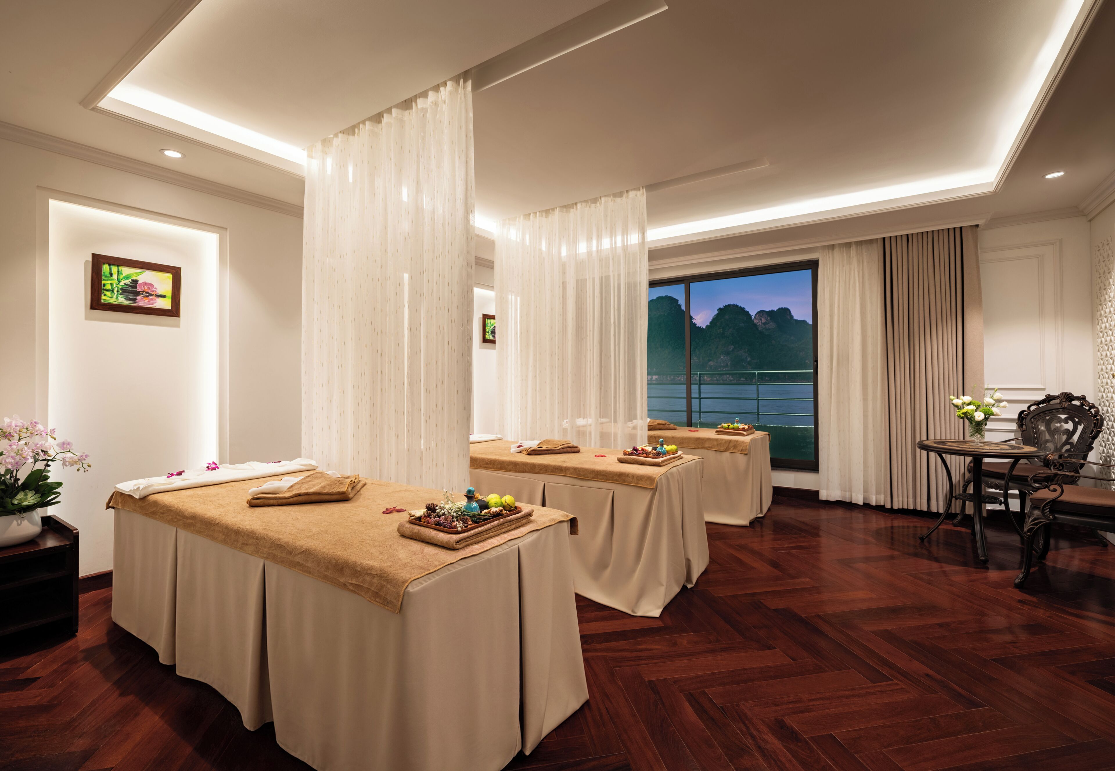 A spa room with three massage tables, a large window with a view, and a small table with flowers.