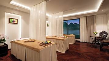 A spa room with three massage tables, a large window with a view, and a small table with flowers.