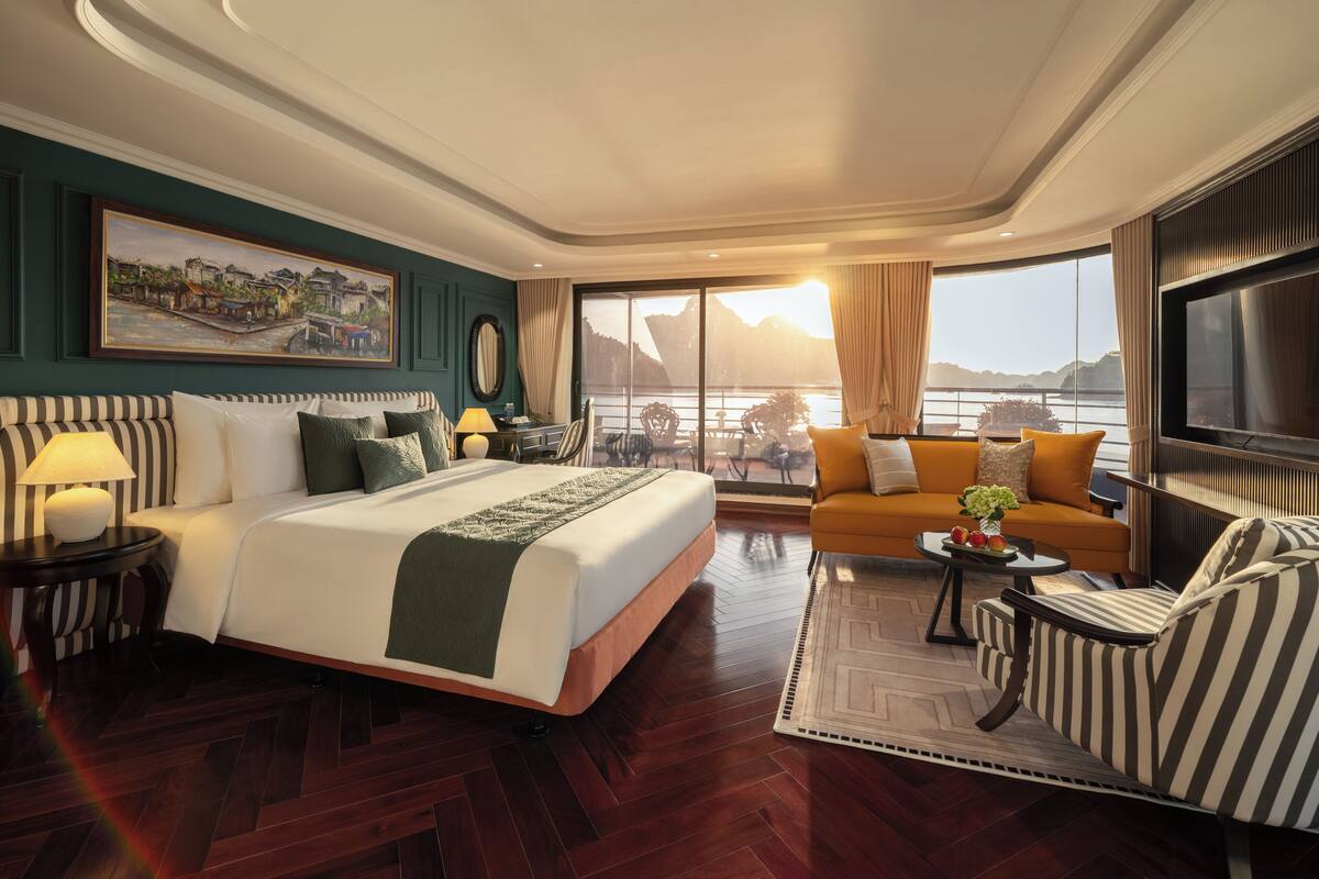 A hotel room with a bed, a sofa, a TV, a desk, and a view of the water.