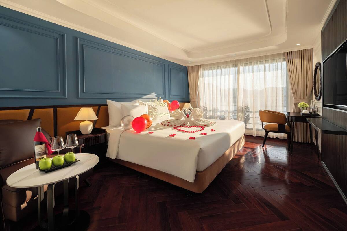 A hotel room with a bed, a desk, a chair, a TV, and a window with curtains.