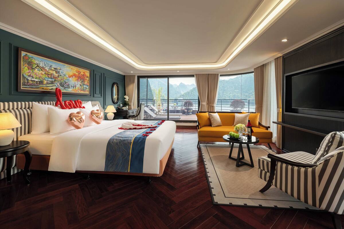 A hotel room with a large bed, a sofa, a TV, a balcony with a view, and a painting on the wall.