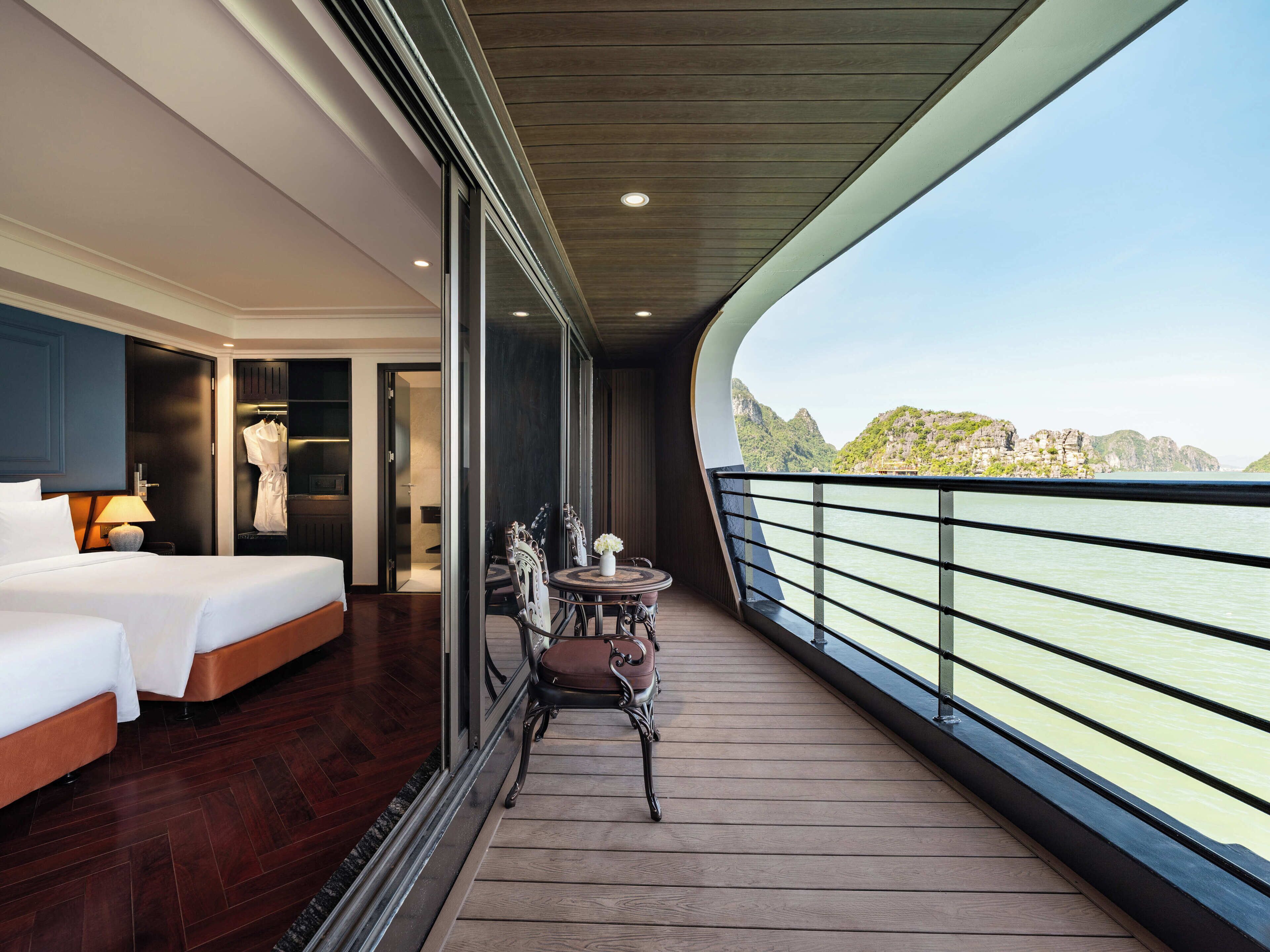 A balcony with a bed, a table with chairs, and a view of the water.