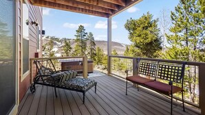 A wooden deck with a metal bench and a cushioned chair, overlooking a mountainous landscape with trees. - Red Barn of Granby Ranch - spacious luxury, pet friendly and hot tub (Granby)